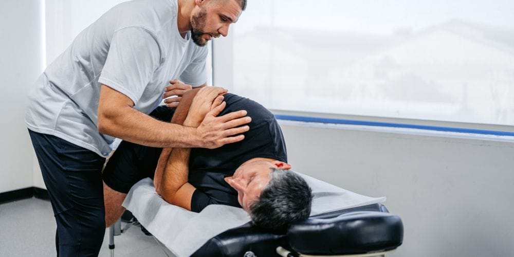 Male chiropractor performing a side-posture spinal adjustment on a patient lying on a treatment table.