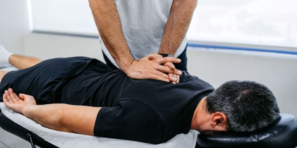 Chiropractor performing a manual spinal adjustment on a male patient lying prone on an examination table