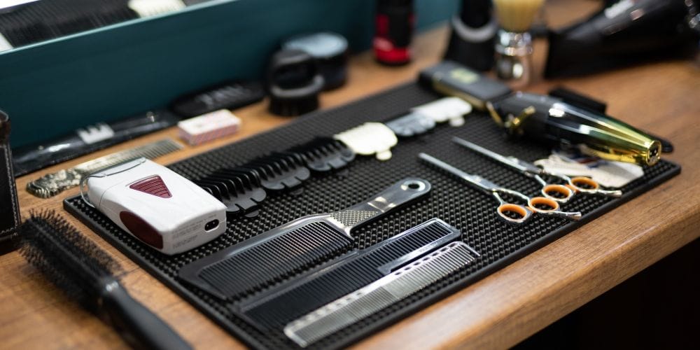 Professional barbershop grooming tools, clippers, shears, and combs neatly organized on a counter mat.