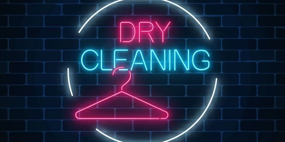 Illuminated neon sign on a dark brick wall displaying the words Dry Cleaning with a clothes hanger icon.