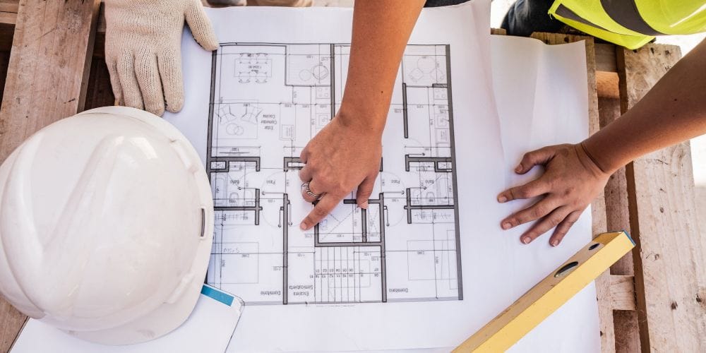 General contractors reviewing residential architectural blueprints on a job site with a hard hat and level