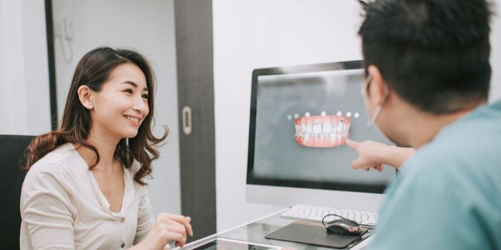 Dentist reviewing a 3D digital teeth scan on a computer screen during a consultation with a smiling female patient